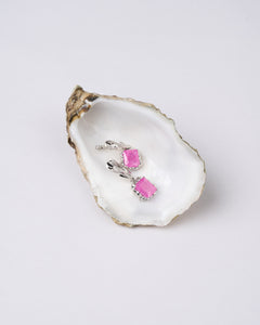 A pair of pink natural Zircon stones earrings set in silver, placed on a white oyster shell.