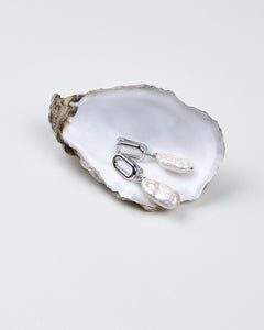 A pair of white baroque pearl earrings with silver geometric clasps, displayed on a white surface.