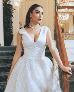 Woman in a white lace dress standing in an elegant interior setting wearing pearls