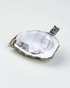 A pair of baroque pearl earrings with sculpted silver clasps, displayed on a oyster shell.