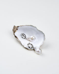 A pair of white baroque pearl earrings with polished silver oval clasps, displayed on a natural oyster shell. Perfect gift for her. 