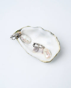 A pair of white pearl earrings with silver-tone latch-back clasps displayed on a white oyster shell. Gift for her
