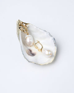 A pair of baroque white pearl earrings with gold-tone latch-back clasps, displayed on a natural oyster shell. Perfect gift for her from Mayfair Pearls.