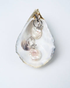 A pair of white baroque pearl earrings with silver-tone latch-back clasps, displayed on a white oyster shell. Gifts for her for weddings and special occasions