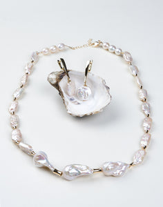 A set of white baroque pearl jewelry with gold accents, including a long necklace and matching earrings displayed on a mannequin head.