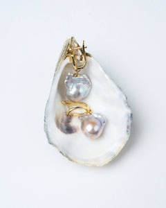 A pair of baroque pearl earrings with gold-tone latch-back clasps displayed on a white oyster shell.