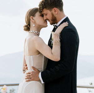 A bride wearing a white baroque pearl necklace and earrings set with gold accents, standing close to a groom.