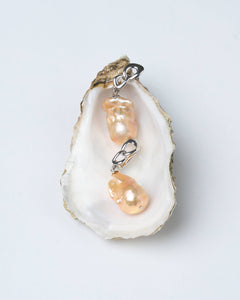 A pair of peach-colored baroque pearl earrings with silver-tone chain-link clasps, displayed on a white surface.