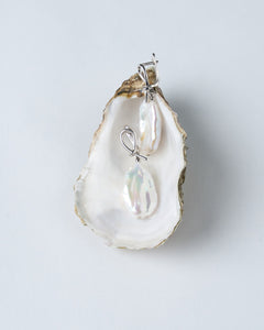A pair of white baroque pearl earrings with silver-tone clasps, displayed in a shell-like setting.
