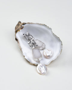 A pair of silver drop earrings with druzy stones and baroque pearl drops displayed on an oyster shell.