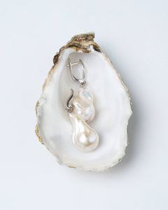A pair of white baroque pearl earrings with silver-tone latch-back clasps and cubic zirconia accents, displayed on a white oyster shell.