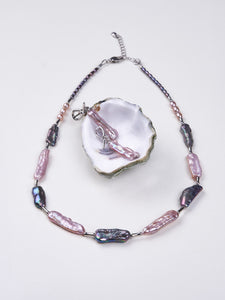 Pink and iridescent stick pearl necklace with matching earrings displayed in oyster shell