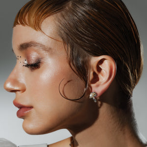 Model is wearing a pair of sculpted wave pearl stud earrings with a silver-tone backdrop and lustrous freshwater pearls.