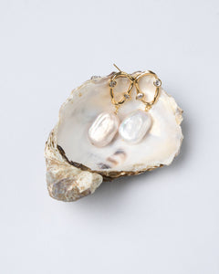 White oval baroque pearl earrings with gold zircon hoops, displayed in oyster shell — Mayfair Pearls jewellery. Perfect gift. 